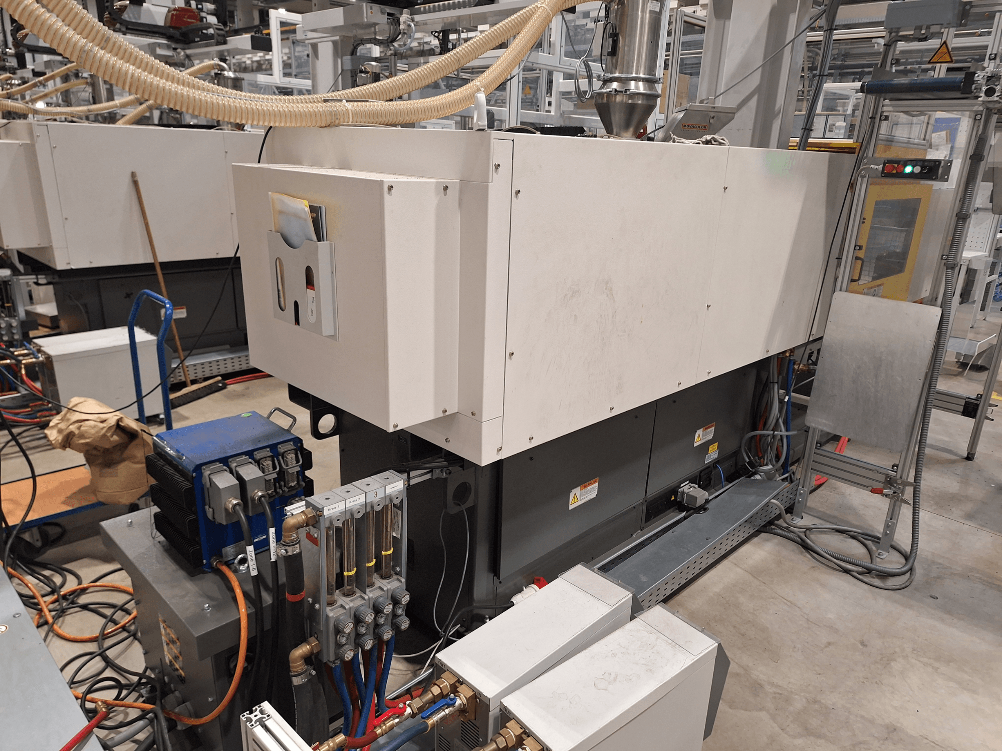 Sprzęt przemysłowy w fabryce; zawiera dużą maszynę z panelem sterowania, wężami i połączeniami elektrycznymi, widok z boku.