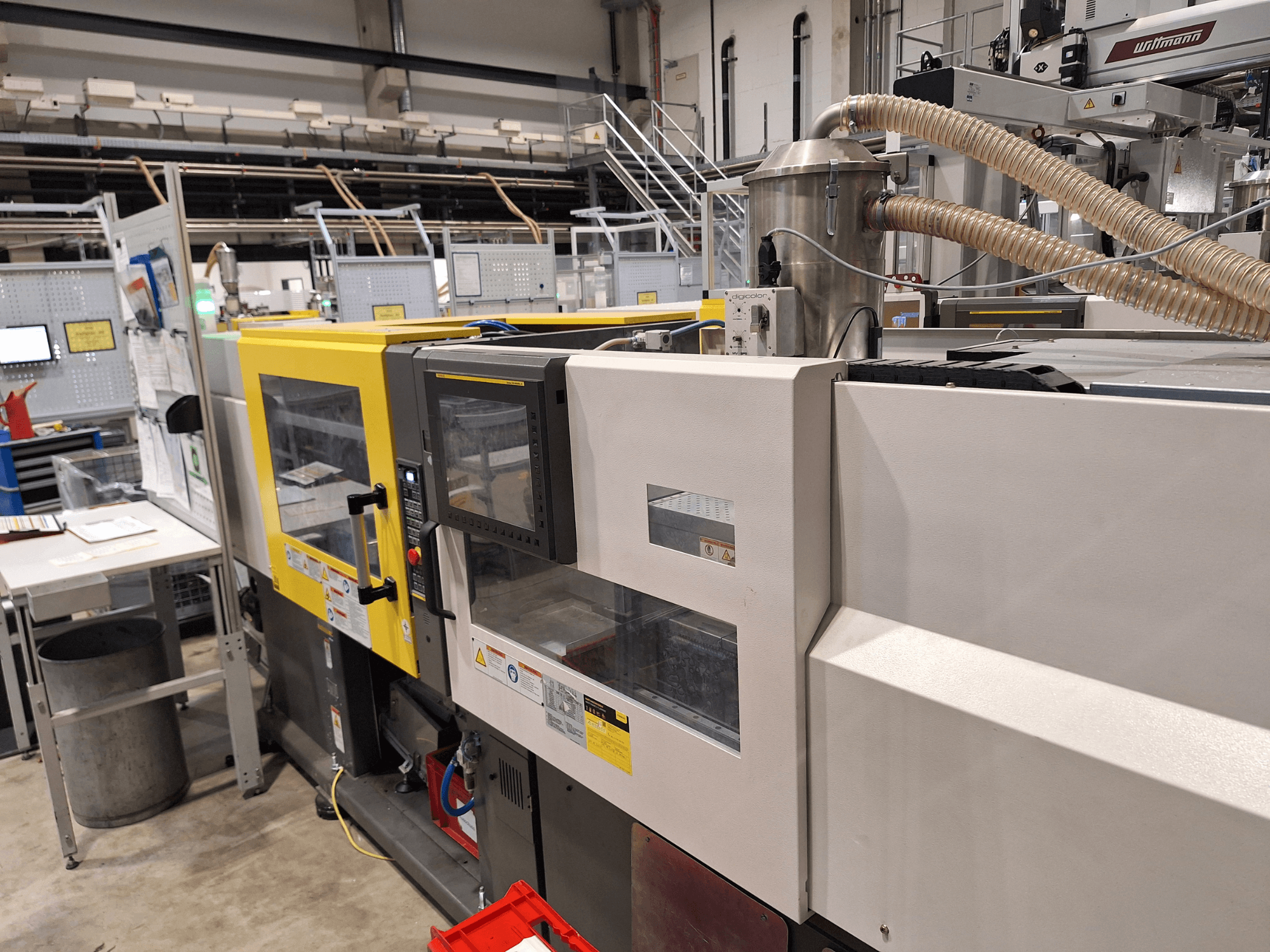 Widok z przodu wielokolorowej wtryskarki z żółtymi i szarymi sekcjami, z panelem sterowania i układem wydechowym.